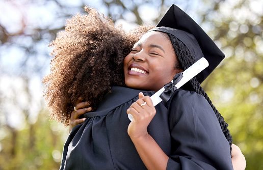 Une jeune diplômée souriante, diplôme à la main, dans les bras d’une proche